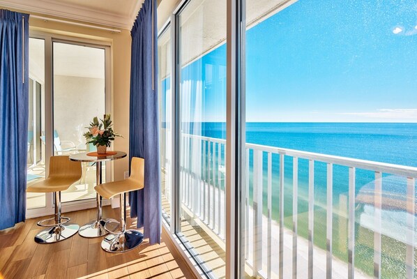 A balcony with a view of the ocean, a table with chairs, and a potted plant.