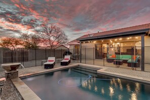 A backyard with a swimming pool, lounge chairs, a barbecue area, and a covered seating area with string lights. - Relaxing 4 Bedroom Home with Sparkling Heated Pool! (Queen Creek)