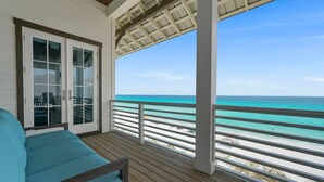 A covered balcony with a view of the beach and ocean.