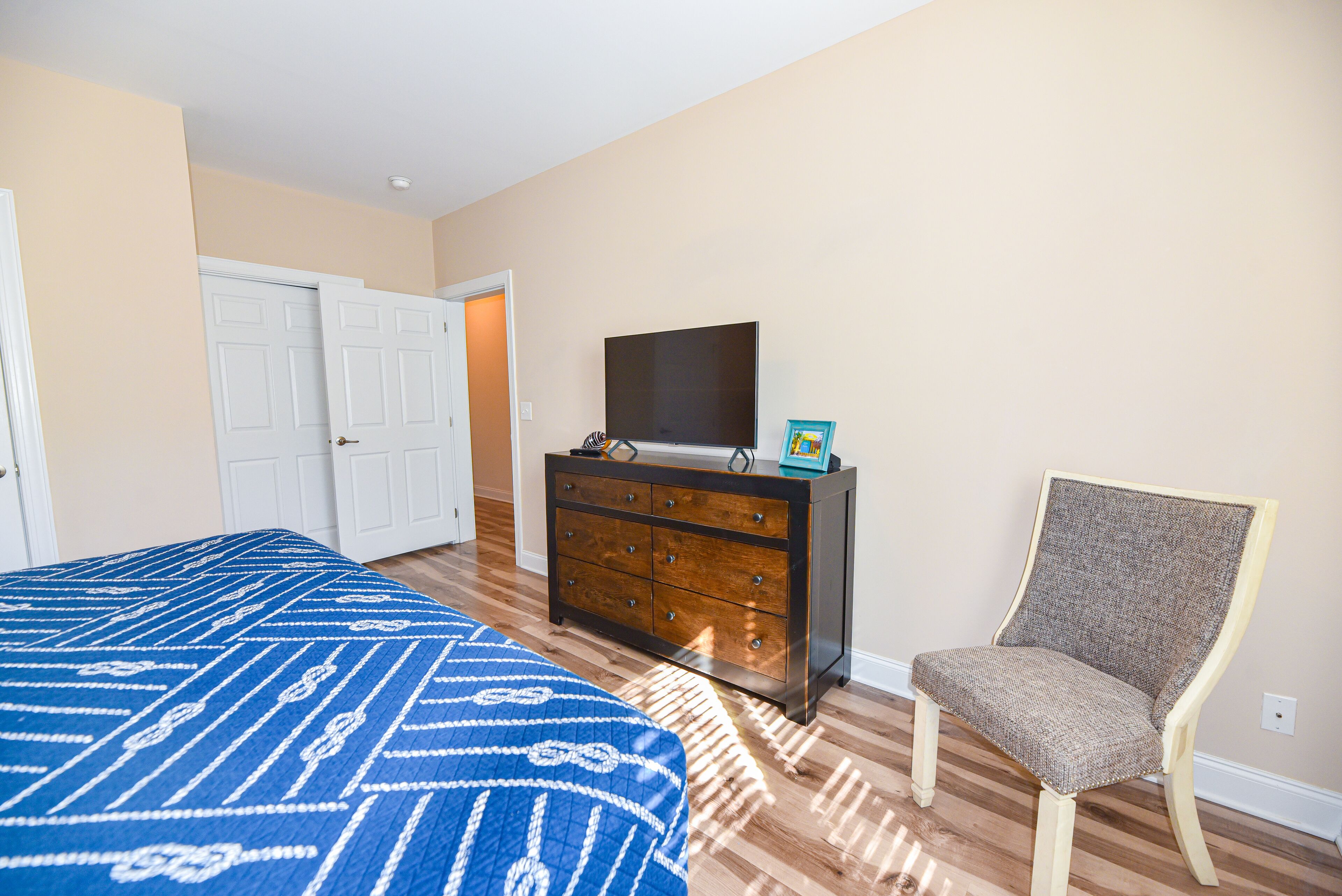 A bedroom with a bed, dresser, TV, and chair.