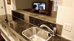 Cocina con encimeras de granito, pileta de acero inoxidable y un televisor al fondo.