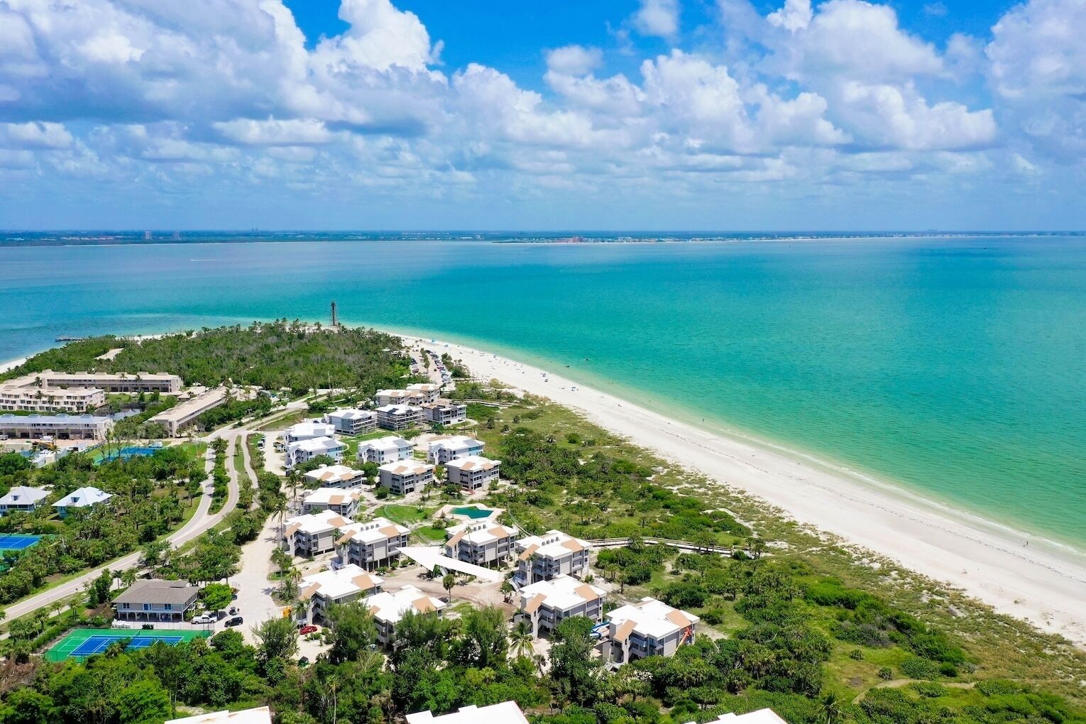 An aerial view of a coastal resort with multiple buildings, a beach, and a clear blue sea.