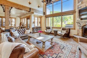A spacious living room with leather sofas, a wooden coffee table, and large windows offering a view of the outdoors. - Mountain Elegance, Location, Luxury -Ski-In-Ski-Out -Village Core - 5 Suites! (Telluride)