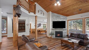 A spacious living room with a stone fireplace, leather sofas, and a wooden ceiling.