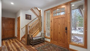 A wooden staircase with a bench, a large wooden door, and a view of a snowy landscape through a window.