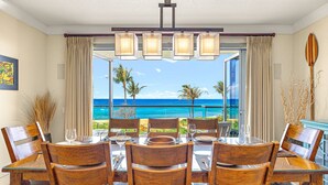 Comedor con mesa preparada para cuatro, con vista a una playa con palmeras y el océano.