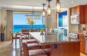 A kitchen with a large island, wooden cabinets, and a view of the ocean. - Maui Resort Rentals Dream Collection: Honua Kai Hokulani 202 – Direct Oceanfront 3BR w/ BBQ on Wraparound Balcony (Lahaina)