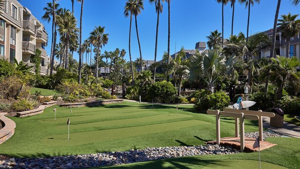 A golf course with a well-maintained green, surrounded by palm trees and a hotel building.