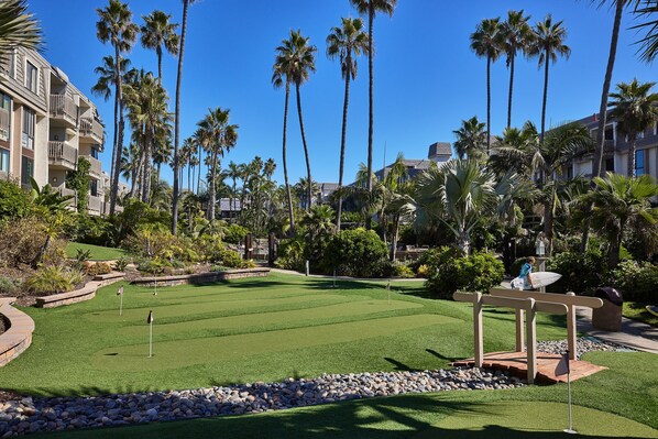 Un campo de golf con un césped bien cuidado, rodeado de palmeras y un edificio de hotel.