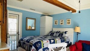 Een slaapkamer met een bed, nachtkastje, dressoir, spiegel en een deur.