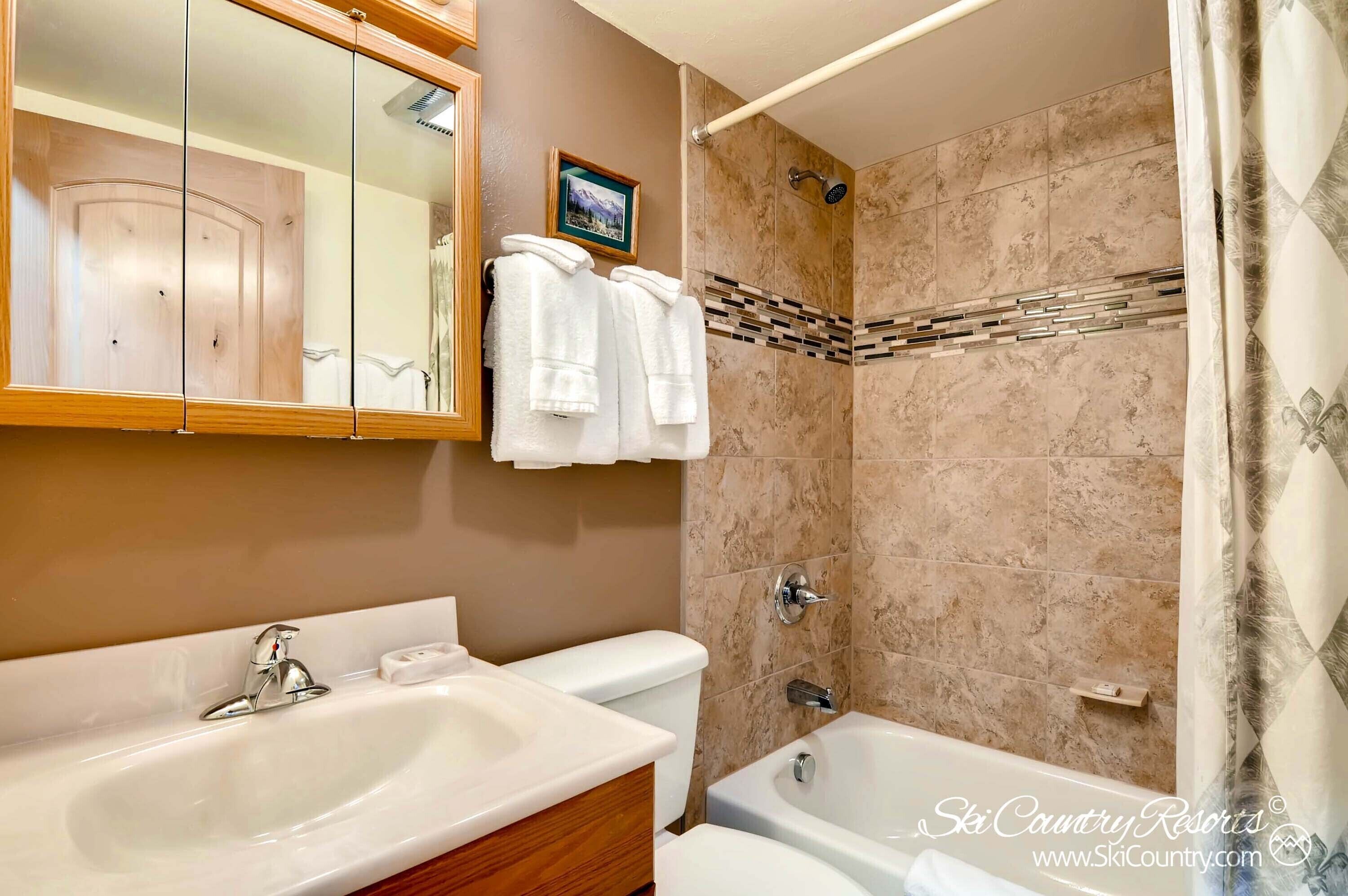 A bathroom with a sink, toilet, and bathtub. There are towels hanging on a rack and a shower with a glass door.