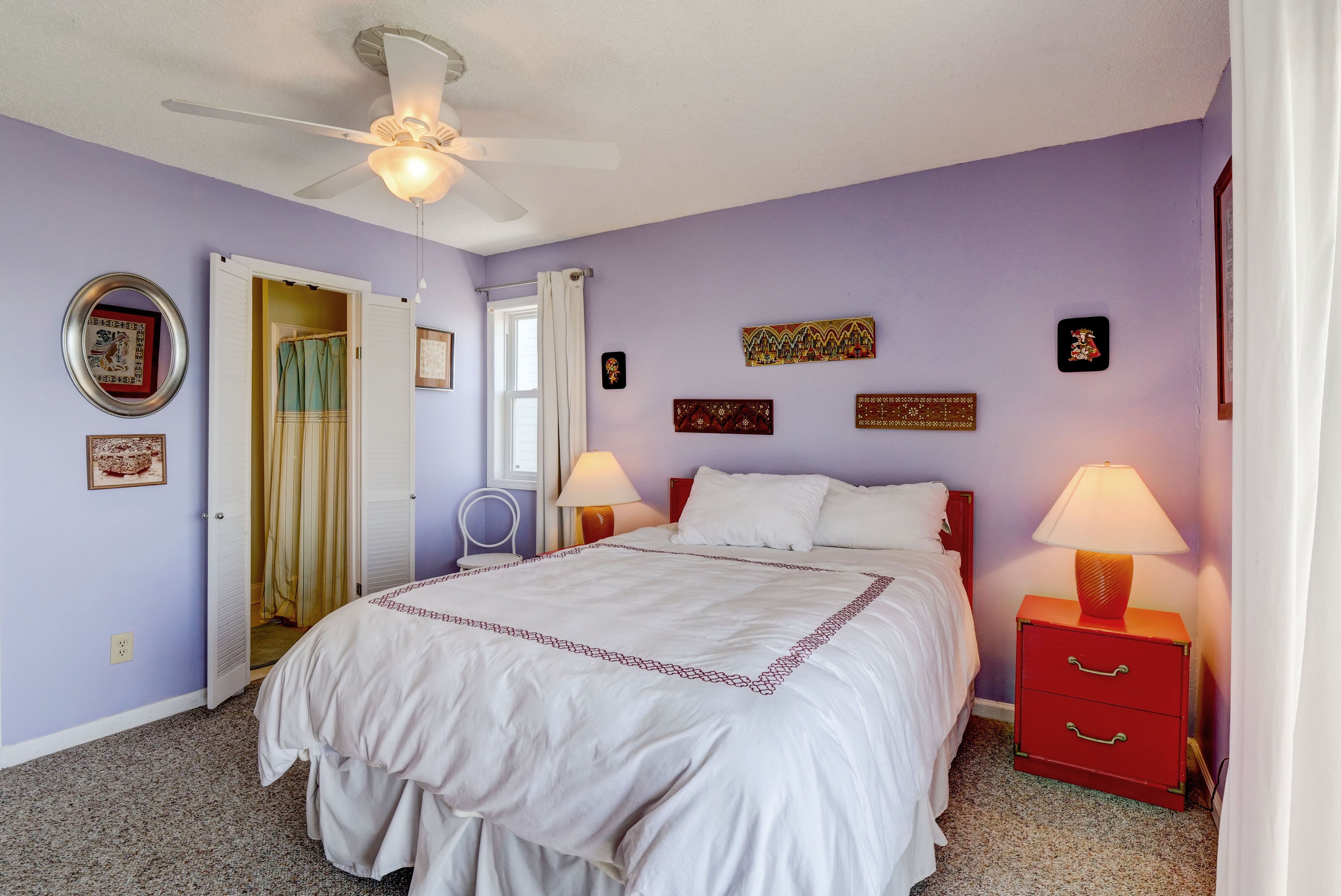 Una camera da letto con un letto, due comodini con lampade, una ventola a soffitto e una porta che dà su un'altra stanza.