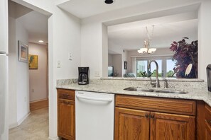 A modern kitchen with granite countertops, a built-in dishwasher, wooden cabinets, and a large window offering a view of the outdoors.