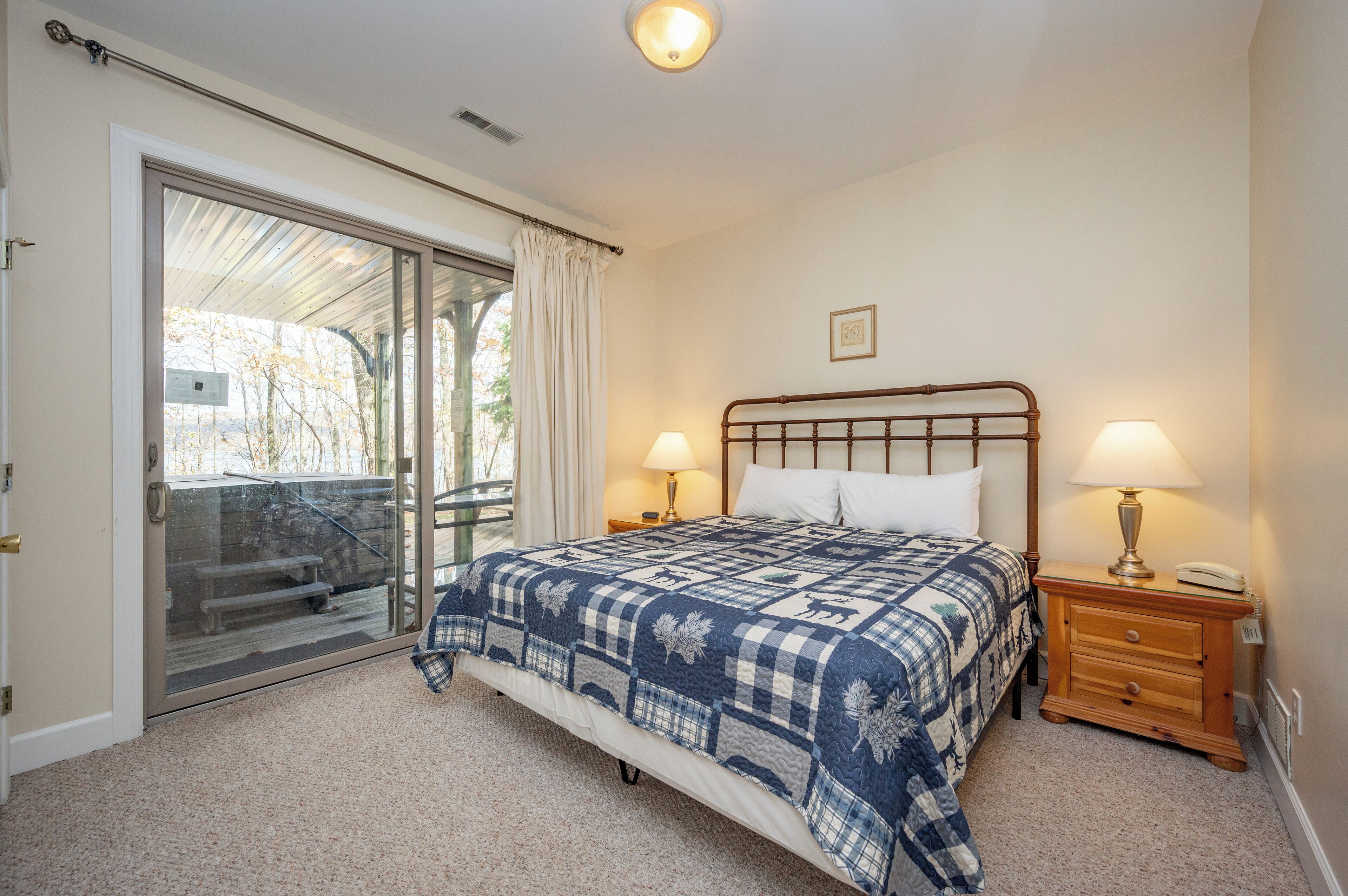 A bedroom with a bed, two bedside tables with lamps, a sliding glass door leading to a balcony, and a small picture on the wall.