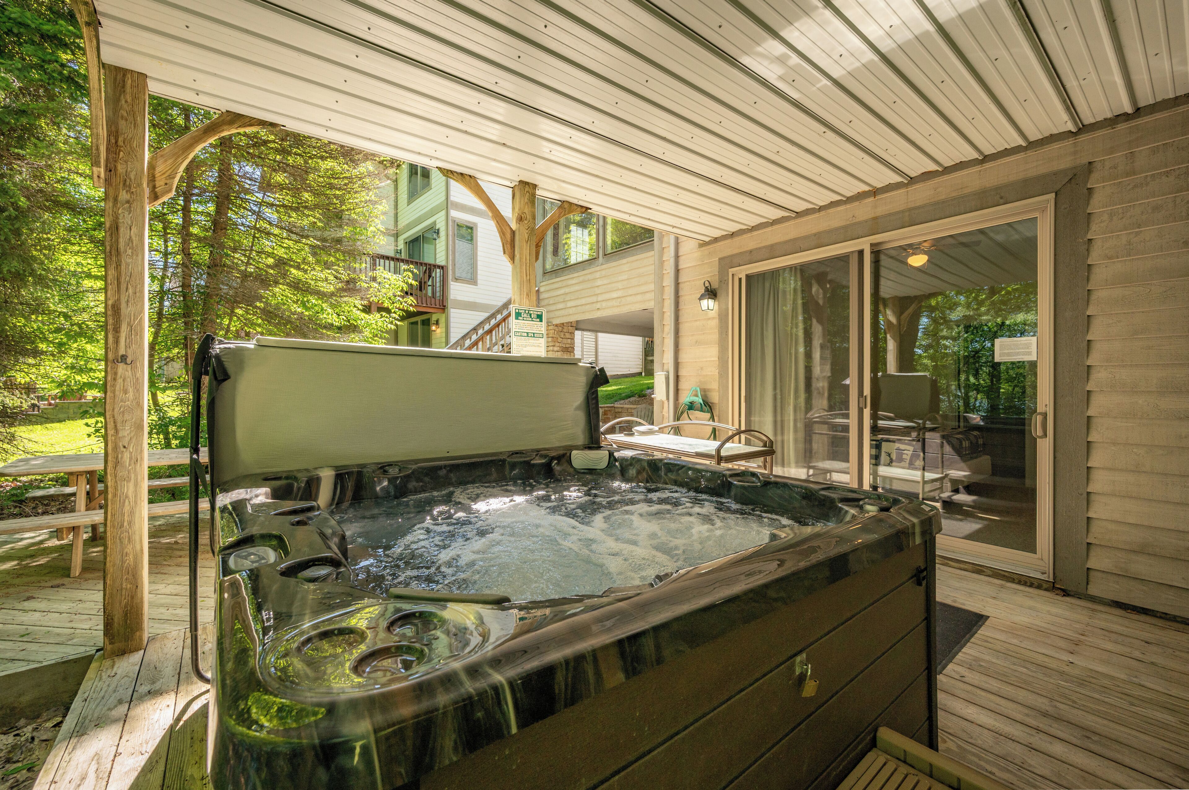 Ein Whirlpool auf einer Holzterrasse mit einer überdachten Veranda und einer Glastür, die zu einem Außenbereich führt.