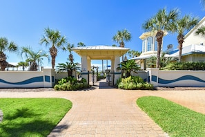 A gated entrance with a covered walkway, palm trees, and a building with a blue and white facade.