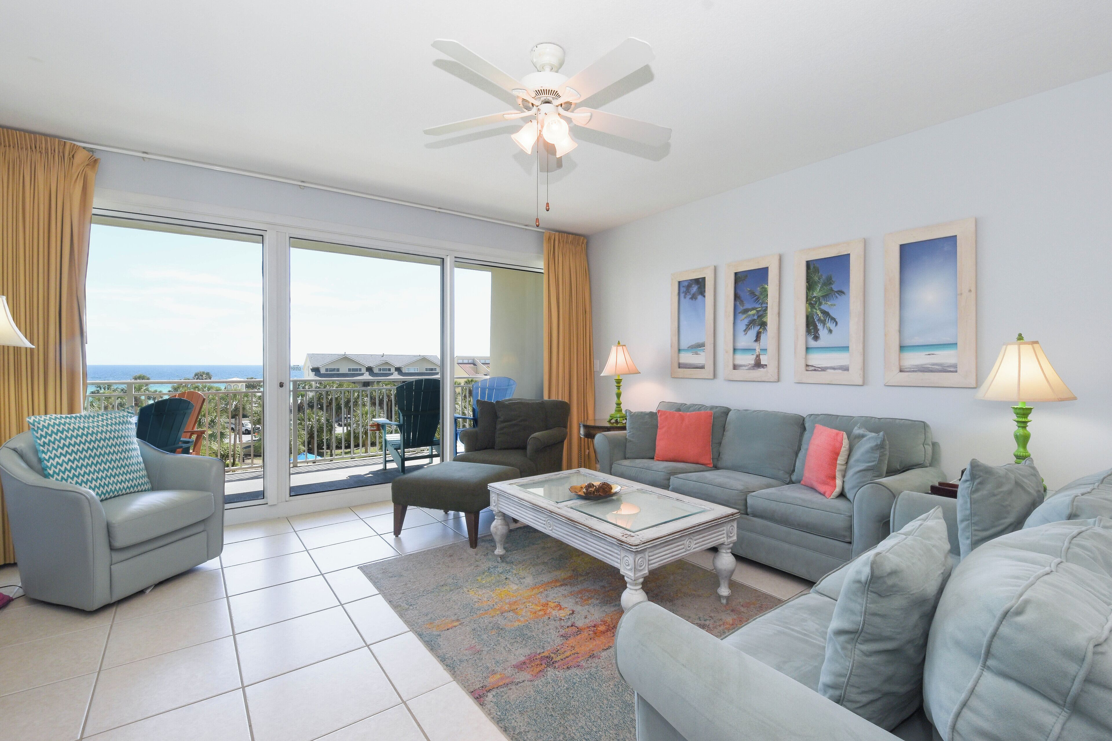 A spacious living room with a balcony, a ceiling fan, and a view of the ocean.