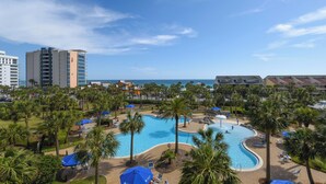 A resort with a large swimming pool surrounded by palm trees and lounge chairs, with a view of the ocean and hotel buildings in the background. - Bright 4th Floor Condo w/ Gulf Views & Modern Touches on Scenic 98 in Destin! 🏖 (Destin)