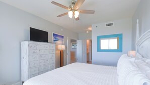 A bedroom with a large bed, a ceiling fan, a dresser, a TV, and a window with a blue frame. - Bright 4th Floor Condo w/ Gulf Views & Modern Touches on Scenic 98 in Destin! 🏖 (Destin)