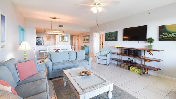 A living room with a sofa, coffee table, and TV. There is a kitchen in the background. - Bright 4th Floor Condo w/ Gulf Views & Modern Touches on Scenic 98 in Destin! 🏖 (Destin)