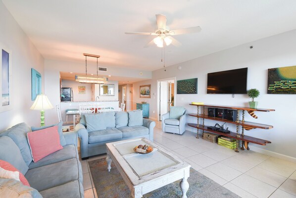 A living room with a sofa, coffee table, and TV. There is a kitchen in the background. - Bright 4th Floor Condo w/ Gulf Views & Modern Touches on Scenic 98 in Destin! 🏖 (Destin)