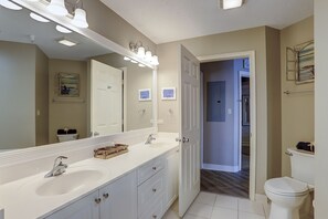 A bathroom with two sinks, a large mirror, and a toilet. There is a door leading to another room. - 1504 SeaCrest - 5th Floor Oceanfront & Stunning Views. (Hilton Head Island)