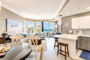A modern kitchen with a central island, a dining area with a round table, and a living room with a sofa and chairs. - 1504 SeaCrest - 5th Floor Oceanfront & Stunning Views. (Hilton Head Island)