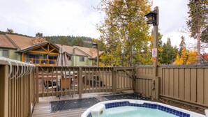 A hot tub area with a wooden deck, a fenced patio, and a view of houses in the background. - Atrium Bluebird Condo: Great Downtown Breck Location (Breckenridge)