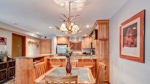 A modern kitchen with wooden cabinets, a central island with seating, and a unique antler chandelier. - Atrium Bluebird Condo: Great Downtown Breck Location (Breckenridge)