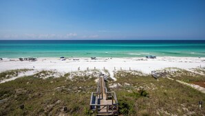 A beach with a wooden boardwalk leading to the water, white sand, and clear turquoise water.