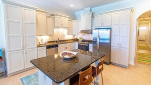 A modern kitchen with white cabinetry, a granite countertop, stainless steel appliances, and a central island with seating.