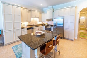 A modern kitchen with white cabinetry, a granite countertop, stainless steel appliances, and a small island with bar stools.