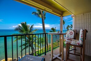 A balcony with a view of the ocean, palm trees, and a chair with floral upholstery.