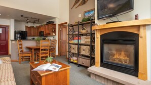 Una sala de estar acogedora con chimenea, muebles de madera, un televisor y una cocina al fondo.
