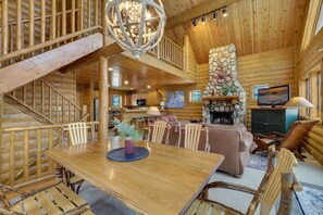 A spacious log cabin interior with a dining area, a fireplace, a television, and a staircase.