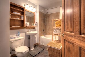 Bathroom features a pedestal sink, bathtub with showerhead, and a wooden shelf for storage.