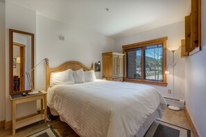 Relax in a spacious bedroom with a large bed, nightstand, and wardrobe, offering a peaceful view of the outdoors.