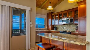 Una cocina con una isla grande, armarios de madera, microondas y vistas a través de un ventanal corredero.