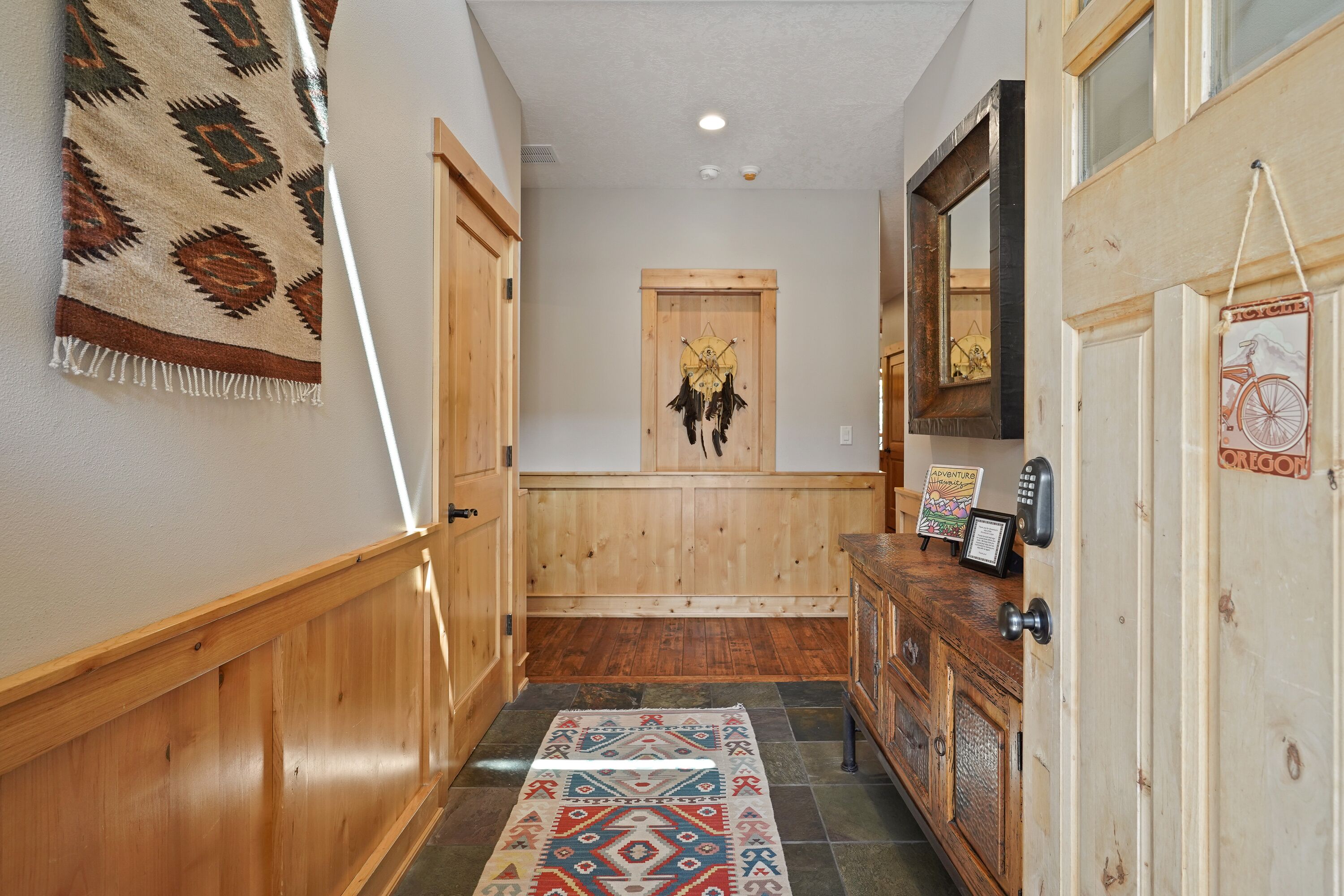 A hallway with wooden walls, a patterned rug, a wooden door with a dreamcatcher, and a cabinet with a bicycle decal.