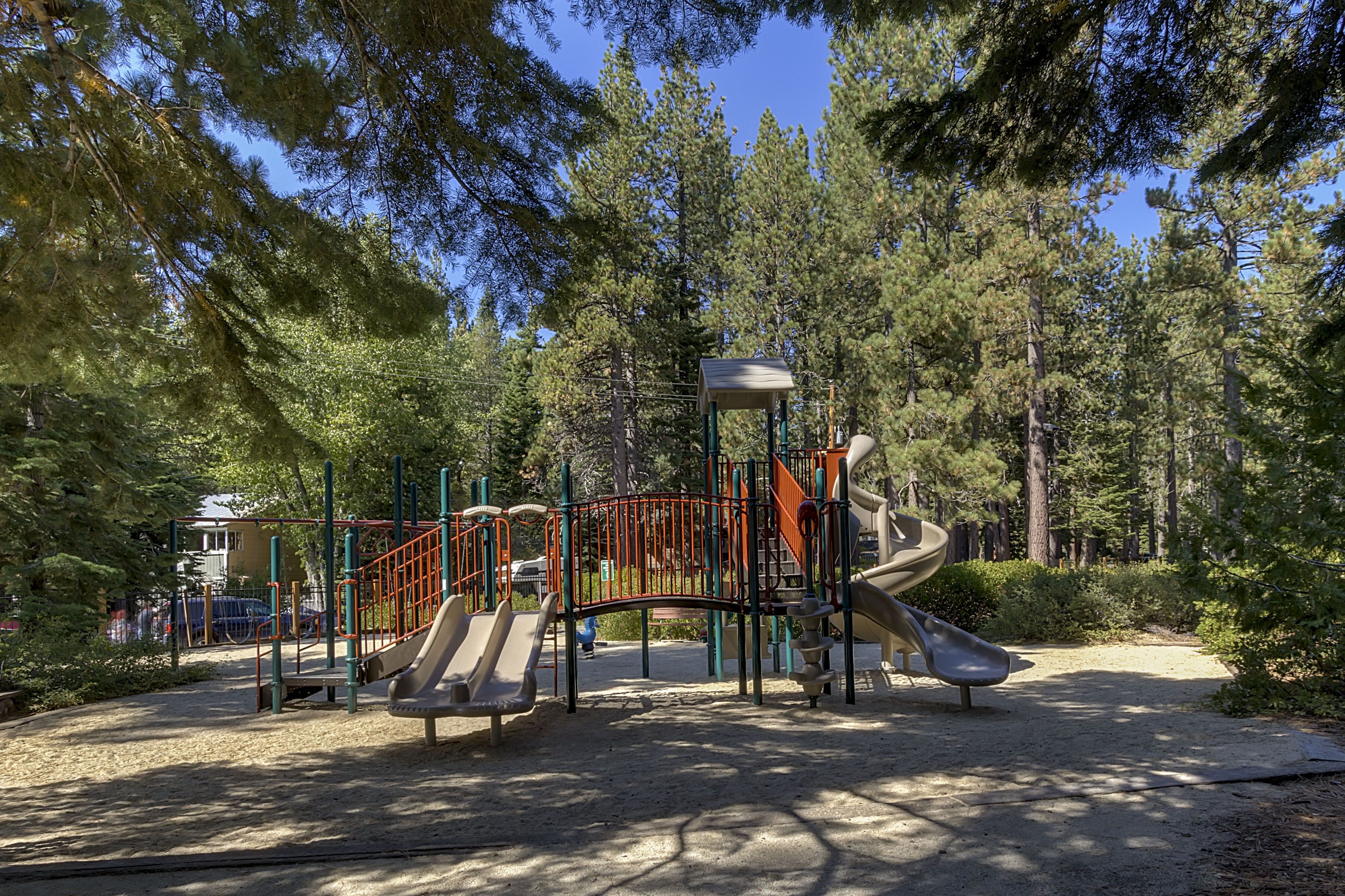 A playground with slides and climbing structures surrounded by trees.