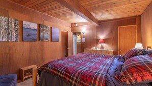 Ein Schlafzimmer mit Holzwandverkleidung, einem Bett, einem Nachttisch, einer Kommode und Wandbildern.