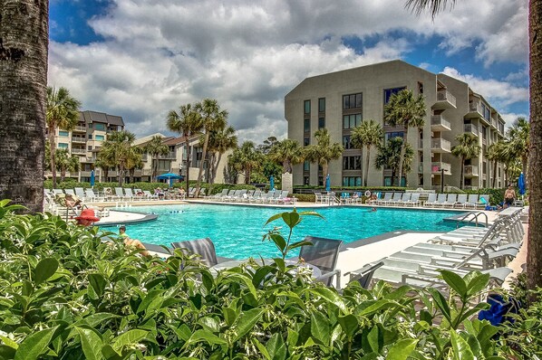 A hotel pool area with multiple swimming pools, lounge chairs, and palm trees.