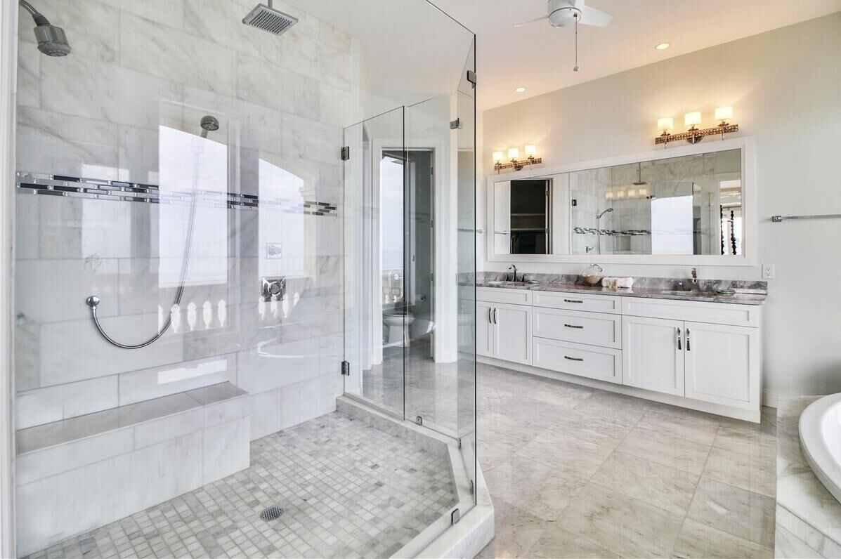 A modern bathroom with a glass-enclosed shower, a large mirror, and a white vanity with drawers.