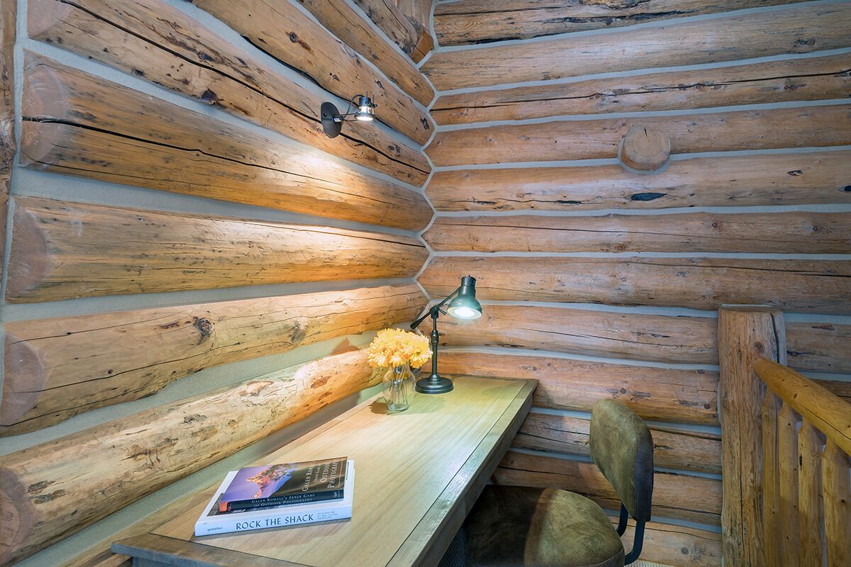 A wooden cabin interior with a desk, a chair, and a lamp.