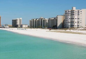 A beachfront hotel with multiple buildings, a sandy beach, and clear turquoise water.
