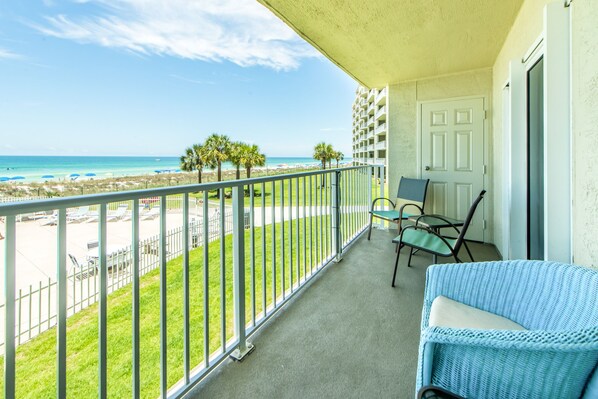 A balcony with a view of the beach, a chair, and a door.