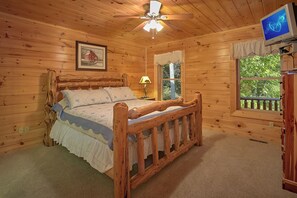 Ein Schlafzimmer einer Holzhütte mit Bett, Deckenventilator, Fenster mit Blick und Fernseher.