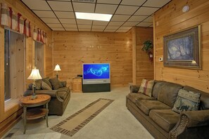 Ein gemütliches Blockhaus-Interieur mit Holzboden, Fernseher, Sofa, kleinem Tisch und Kamin.