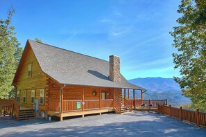 Eine Blockhütte mit einem Steinofen, einer Holzterrasse und Blick auf die Berge.