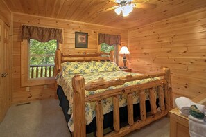 A wooden cabin bedroom with a bed, a nightstand, a lamp, and a window with curtains. - Cabin w/Private Pool-Theater-Mountain View-Game Room (GATLINBURG)